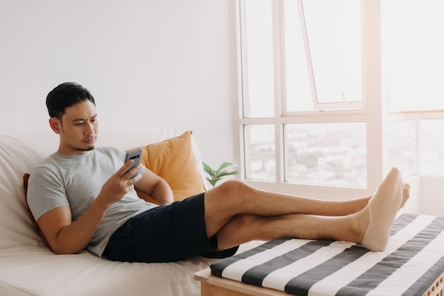 Man kijkt naar zijn mobiel terwijl hij ontspant op de bank in zijn woonkamer