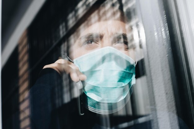 Man kijkt uit het raam terwijl hij telefoneert met een medisch masker