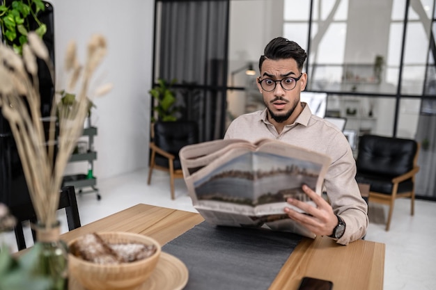 Man kijkt verbaasd naar de krant aan tafel