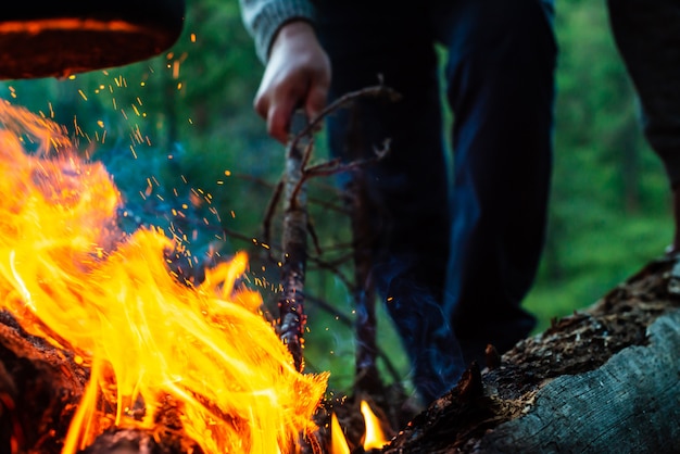 男は森でたき火を燃やします。キャンプファイヤーの大気炎がクローズアップ。自然でのキャンプ。アクティブな休息。レクリエーション野外。 Copyspaceと煙で美しいオレンジ色の火。