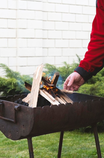 a man kindles a fire in the barbecue in the backyard