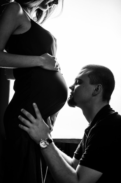 A man kisses his pregnant wife on the stomach Black and white photo