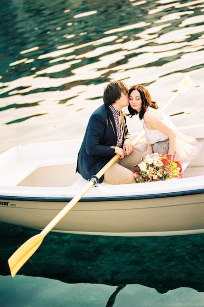 Man kisses woman on the cheek while sitting in a boat with oars