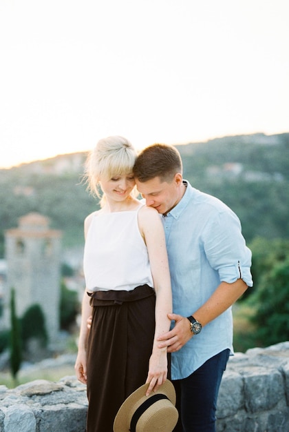 Man kisses woman on the shoulder hugging her from behind on a background of mountains