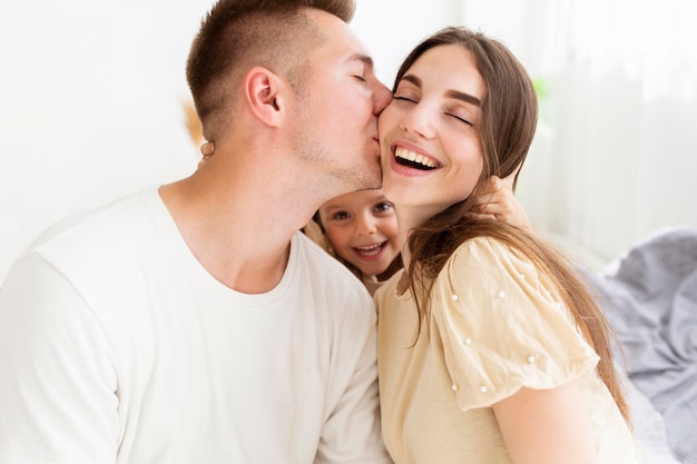 Foto uomo che bacia la moglie sulla guancia accanto alla figlia