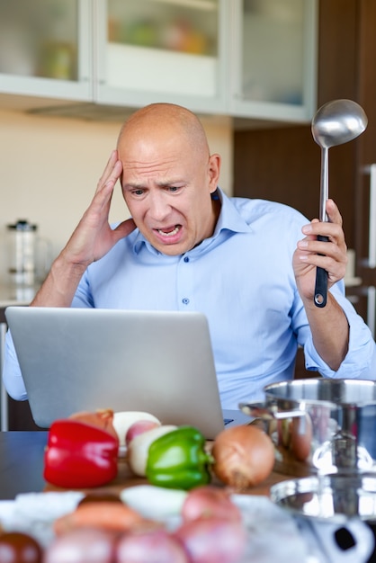 Man in kitchen looking for recipes on his laptop. Cooking in home, online.