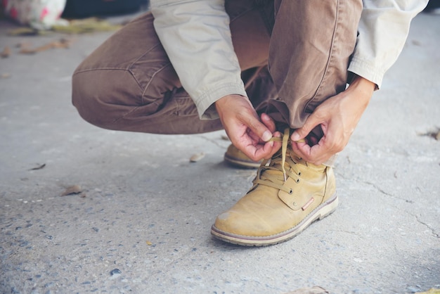 写真 男はひざまずいて、労働者のための靴産業のブーツを結ぶ彼の建設のために靴ひもを結んだ男の手のショットを閉じる茶色のブーツ靴のコンセプトのために男の手を縛る靴を閉じる
