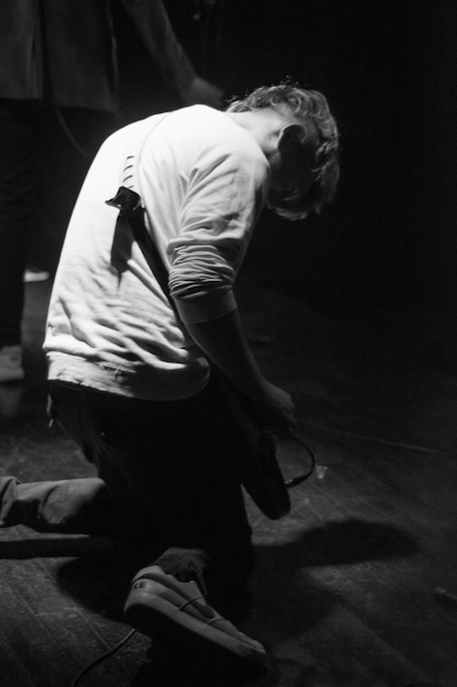 A man kneeling on a stage with a guitar on his knee.