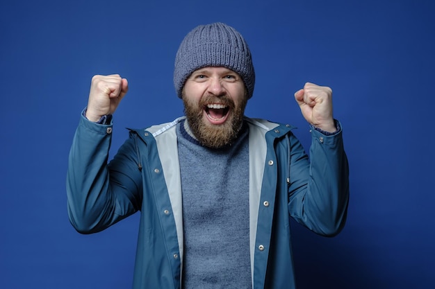 Foto uomo con cappello lavorato a maglia e giacca impermeabile molto felice fa un gesto con le mani e urla