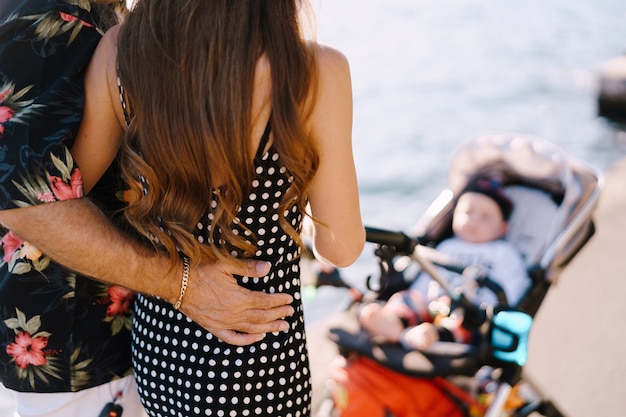 Man knuffelt vrouw voor een kinderwagen met een baby achteraanzicht