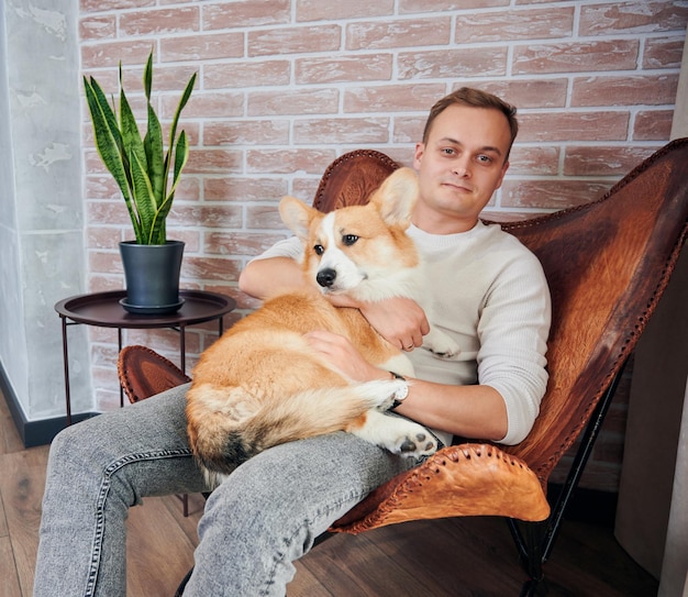 Man knuffelt zijn hondje terwijl hij thuis in een leunstoel rust