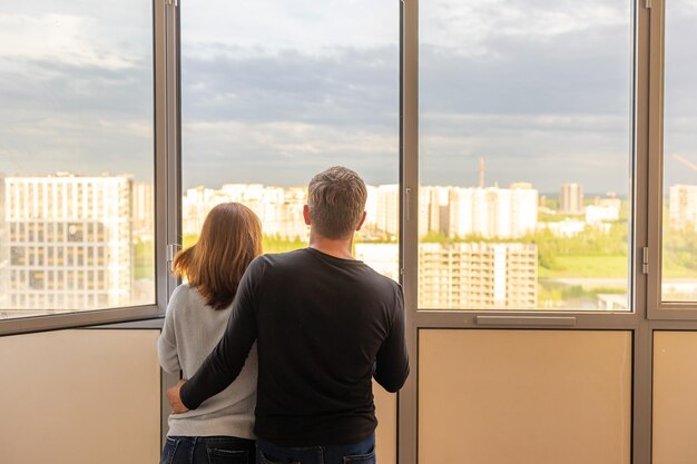 Man knuffelt zijn vrouw Jong stel verhuist naar een nieuw appartement Mensen kijken uit het raam naar nieuwe huizen Concept nieuwe huizen nieuw begin