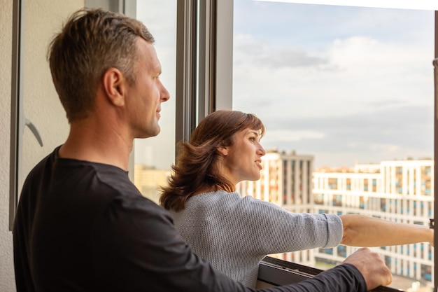 Man knuffelt zijn vrouw Jong stel verhuist naar een nieuw appartement Mensen kijken uit het raam naar nieuwe huizen Concept nieuwe huizen nieuw begin