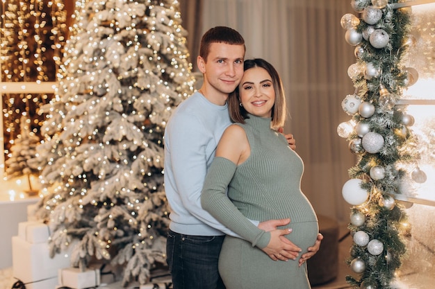 man knuffelt zwangere vrouw in de buurt van kerstboom