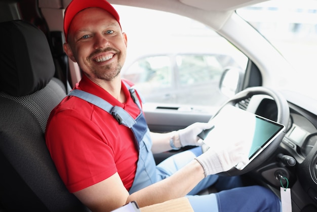 Man koerier zit achter het stuur van de auto en houdt digitale tablet in zijn handen