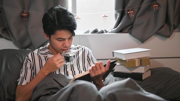 Man koffie drinken en een boek lezen op zijn bed in de ochtend