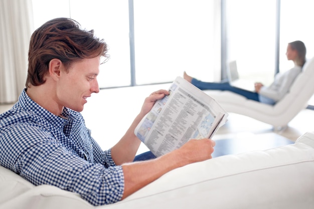 Man krant en lezen op de bank met ontspanning voor verhaal artikel of informatie met glimlach in de woonkamer Persoon nieuws en ochtendroutine op de sofa met gedrukte media of kennis voor pauze in de lounge