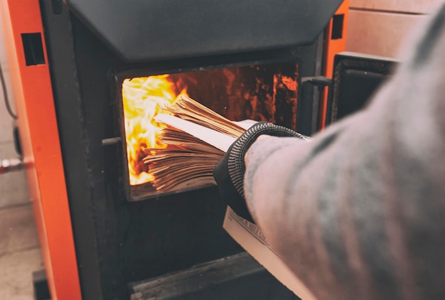 Man laadt de oude kranten in de vaste brandstofketel in de stookruimte Vaste brandstof en verwarmingsconcept