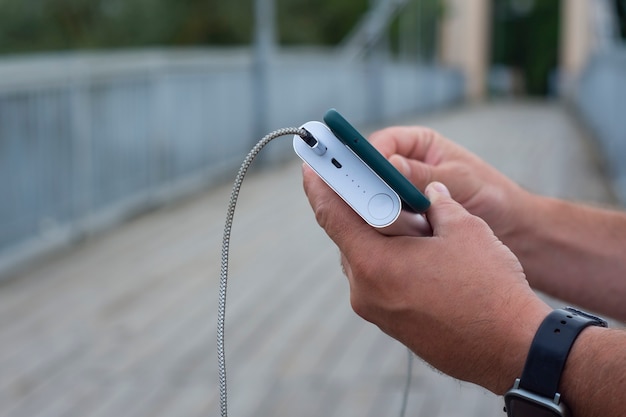 Man laadt een smartphone op met een powerbank in de hand. draagbare oplader voor het opladen van gadgets.