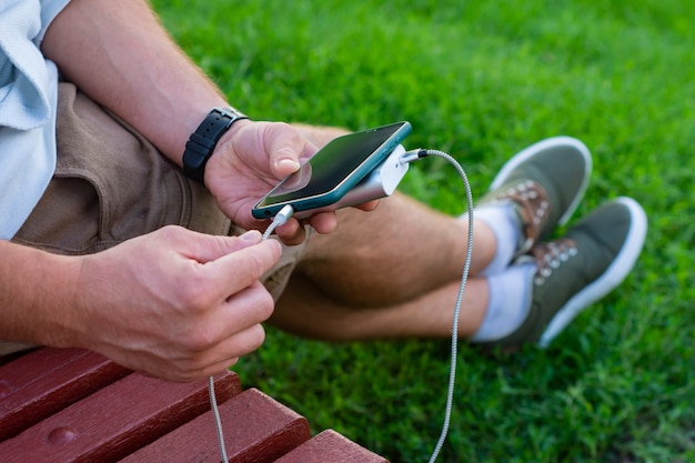 Man laadt een smartphone op met een powerbank in de hand. Draagbare oplader voor het opladen van gadgets.