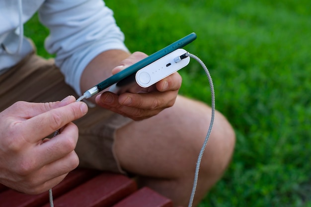 Man laadt een smartphone op met een powerbank in de hand. Draagbare oplader voor het opladen van gadgets.