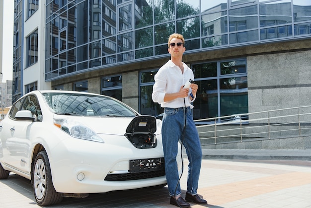 Man laadt zijn luxe elektrische auto op bij een buitenstation voor moderne nieuwe stadsgebouwen