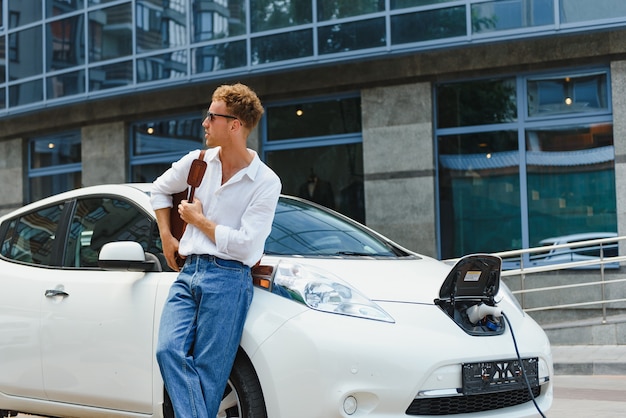 Man laadt zijn luxe elektrische auto op bij een buitenstation voor moderne nieuwe stadsgebouwen