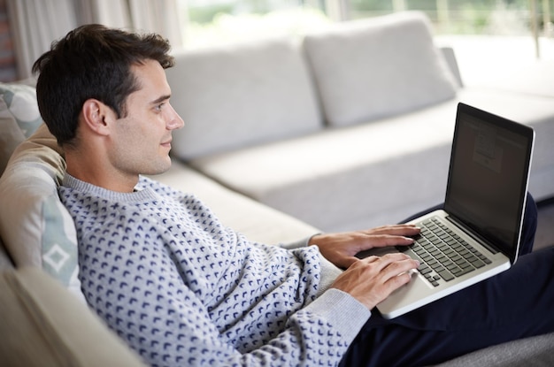 Man laptop en bank in de woonkamer voor tech sociale media en onderzoek voor thuis of binnen in het weekend Mannelijke persoon en glimlachen met de hand op het toetsenbord voor browsen type en scherm met internet en online