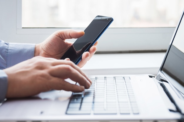 Man behind laptop with smartphone