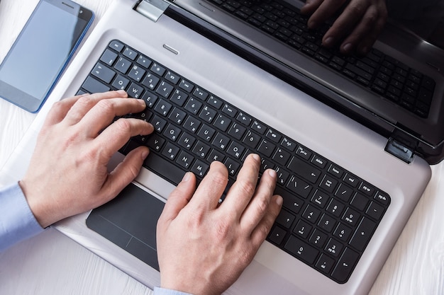 Man behind laptop with smartphone