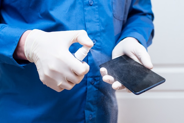 Человек в латексных перчатках дезинфицирует телефон с помощью дезинфицирующего средства