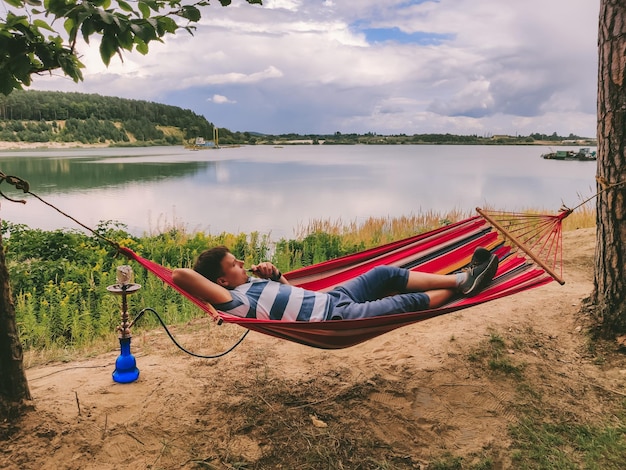 Фото Мужчина лежит в гамаке и курит кальян, глядя на пляж озера