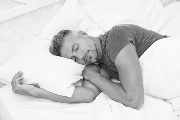 Foto uomo sdraiato sul letto sveglio che dorme in un letto comodo buongiorno semplicemente rilassante uomo del sonno uomo barbuto che dorme sul letto nella camera da letto uomo a letto buon pisolino uomo con gli occhi chiusi mentre si rilassa