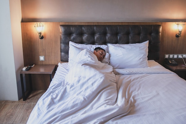 Man laying on bed covered with blanket while sleeping on white sheets