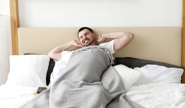 A man laying in bed with a grey blanket that says'i'm a good man '