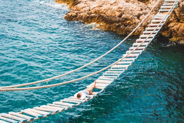 Человек, лежащий на подвесном мосту, наслаждаясь видом на море и спокойствием природы в летнее время