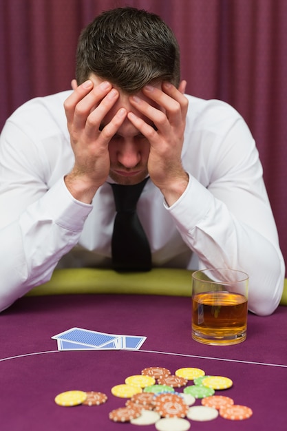 Man leaning on poker table looking worried in casino