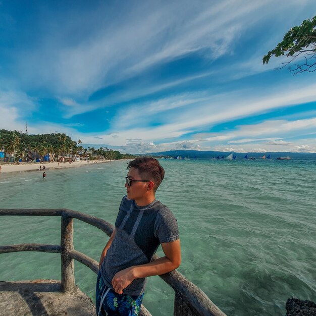 Photo man leaning on railing by sea against sky