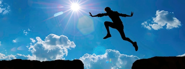 Photo man leaping across a chasm in silhouette against a backdrop of the blue sky and sun