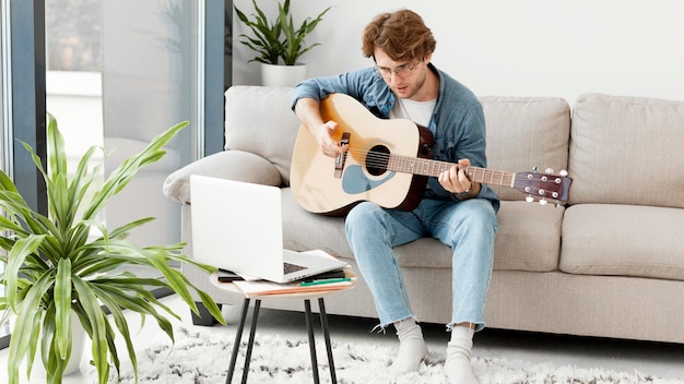 Photo man learning guitar online and sitting on sofa