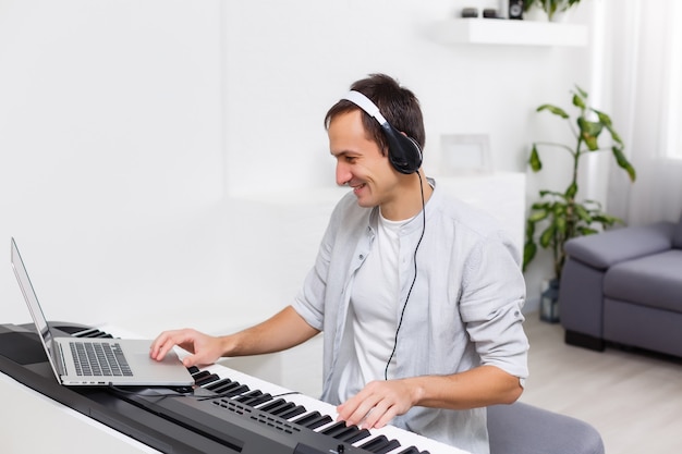 Мужчина учится играть на пианино онлайн с компьютером, оставаясь дома. Концепции самоучки, пребывания дома и работы в Интернете