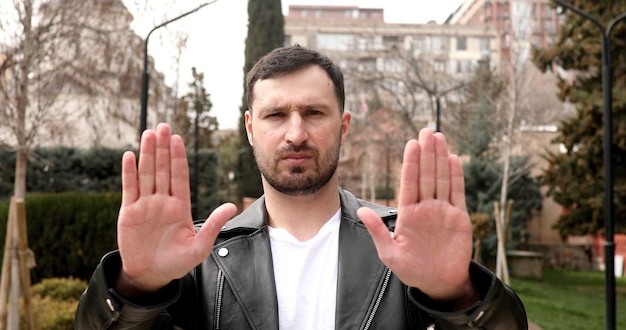 A man in a leather jacket holds up his hands to show the word " stop ".