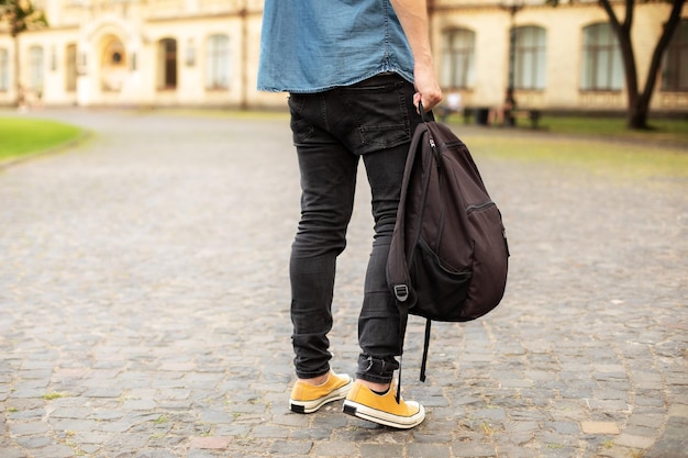 Man legs in yellow sneakers, denim shirt, jeans at university campus. Back view of stylish man