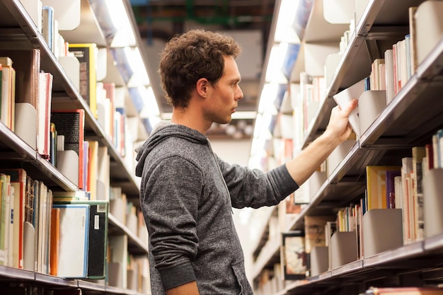 A man in a library is looking at a book shelf.