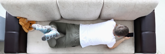 Man lie on sofa and hold modern smartphone in hand