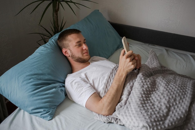 男はベッドに横になり、彼のスマートフォンを見ます