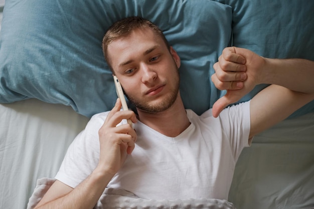 A man lies in bed and talks on the phone upset