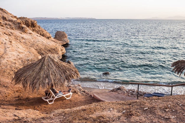 Photo man lies on a lounger against the background of the sea and sandy beach