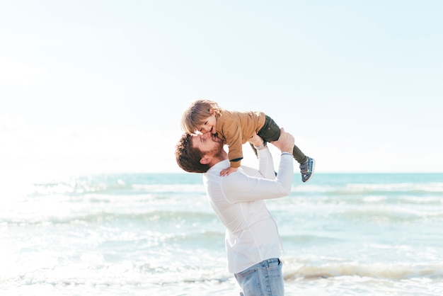 Man lifting baby boy up on seashore