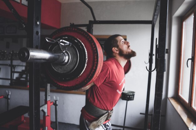 Foto uomo che solleva una barra mentre si esercita in palestra